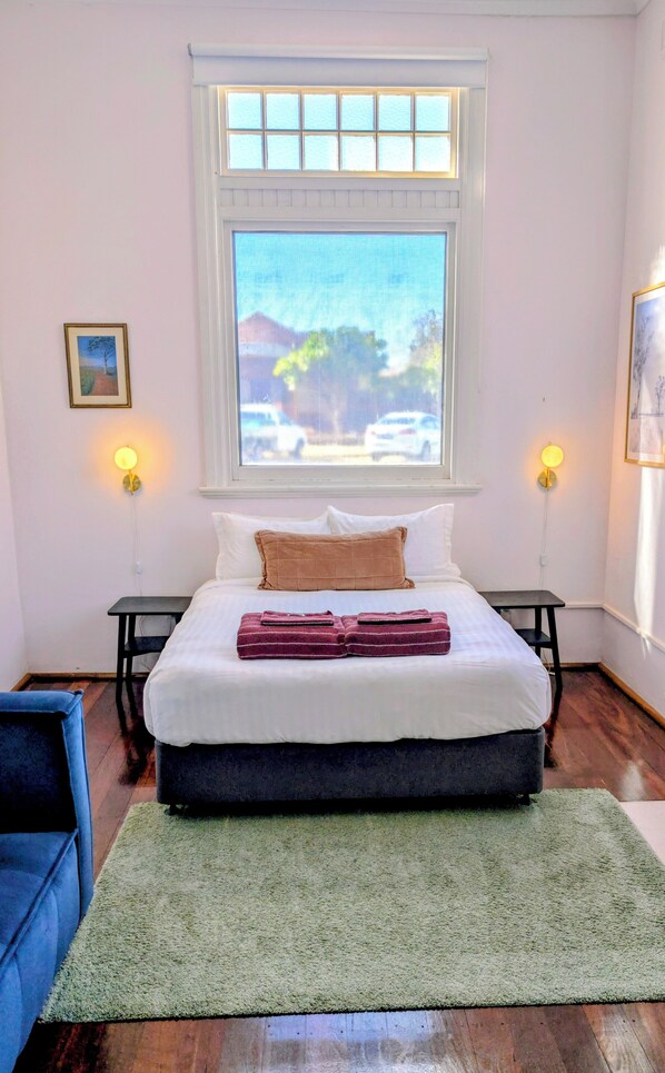 Une chambre avec une grande fenĂȘtre, un lit avec une literie blanche et marron, deux tables de chevet avec des lampes et un tapis vert.