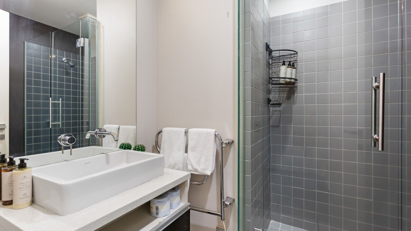 Un baño moderno con ducha de vidrio, lavamanos blanco y espejo.