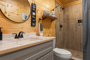 Een badkamer met houten lambrisering, een wastafel met kraan, een toilet, een douchegedeelte en een plank met een fles en een bord.'