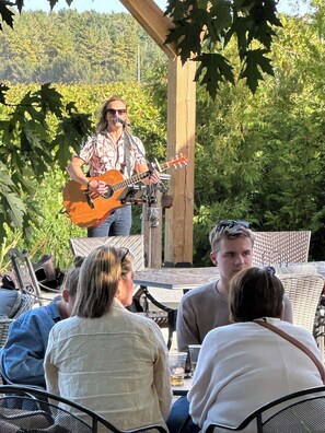 A person playing a guitar at an outdoor event with a group of people seated at tables. - Vineyard Escape Near Bayfield (Bayfield)