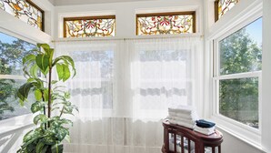 Ein Zimmer mit großem Fenster, einer Topfpflanze und einem kleinen Tisch mit zusammengelegten Handtüchern.
