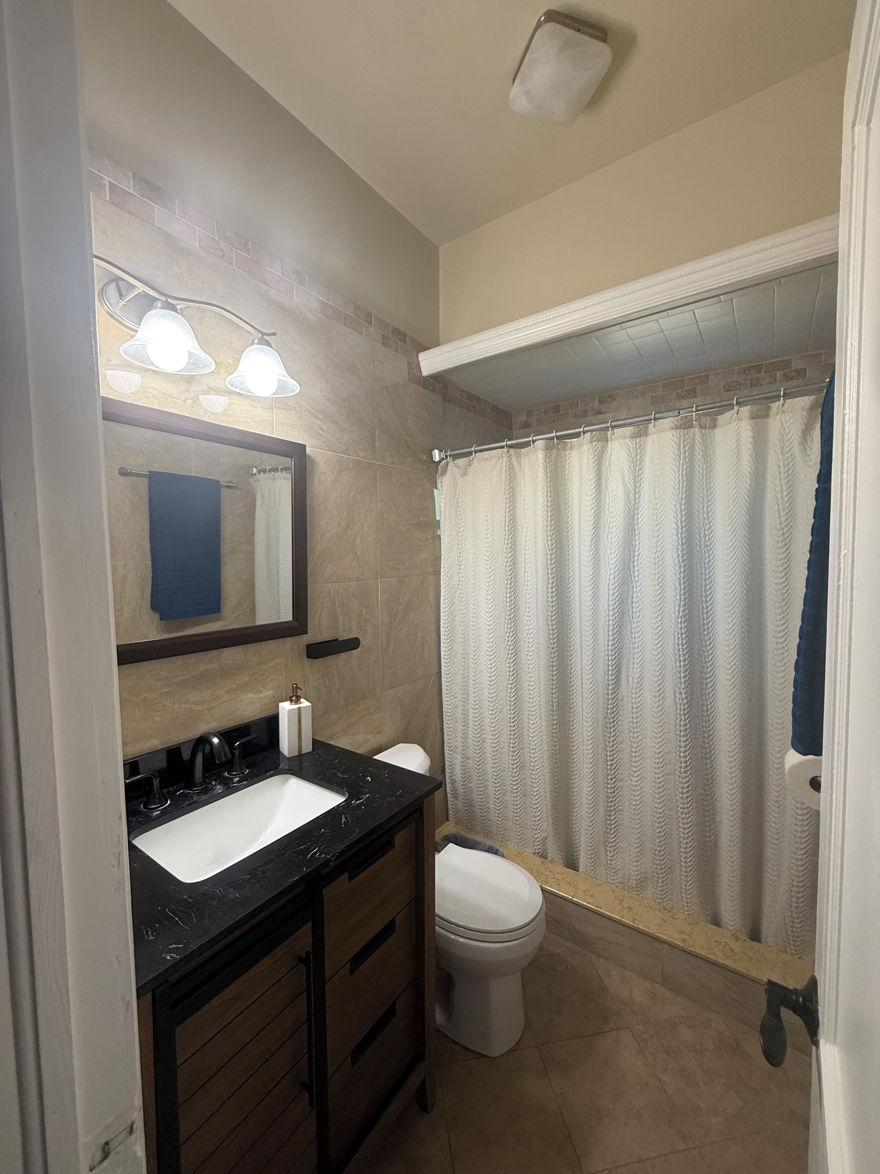 A bathroom with a sink, mirror, towel rack, toilet, and shower curtain.. Eirini’s Home