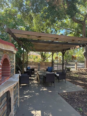Un patio al aire libre con horno de ladrillo, mobiliario de mimbre y una pérgola.