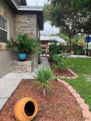 A residential property with a stone and brick exterior, a small garden with mulch, a palm plant, and a tire planter.