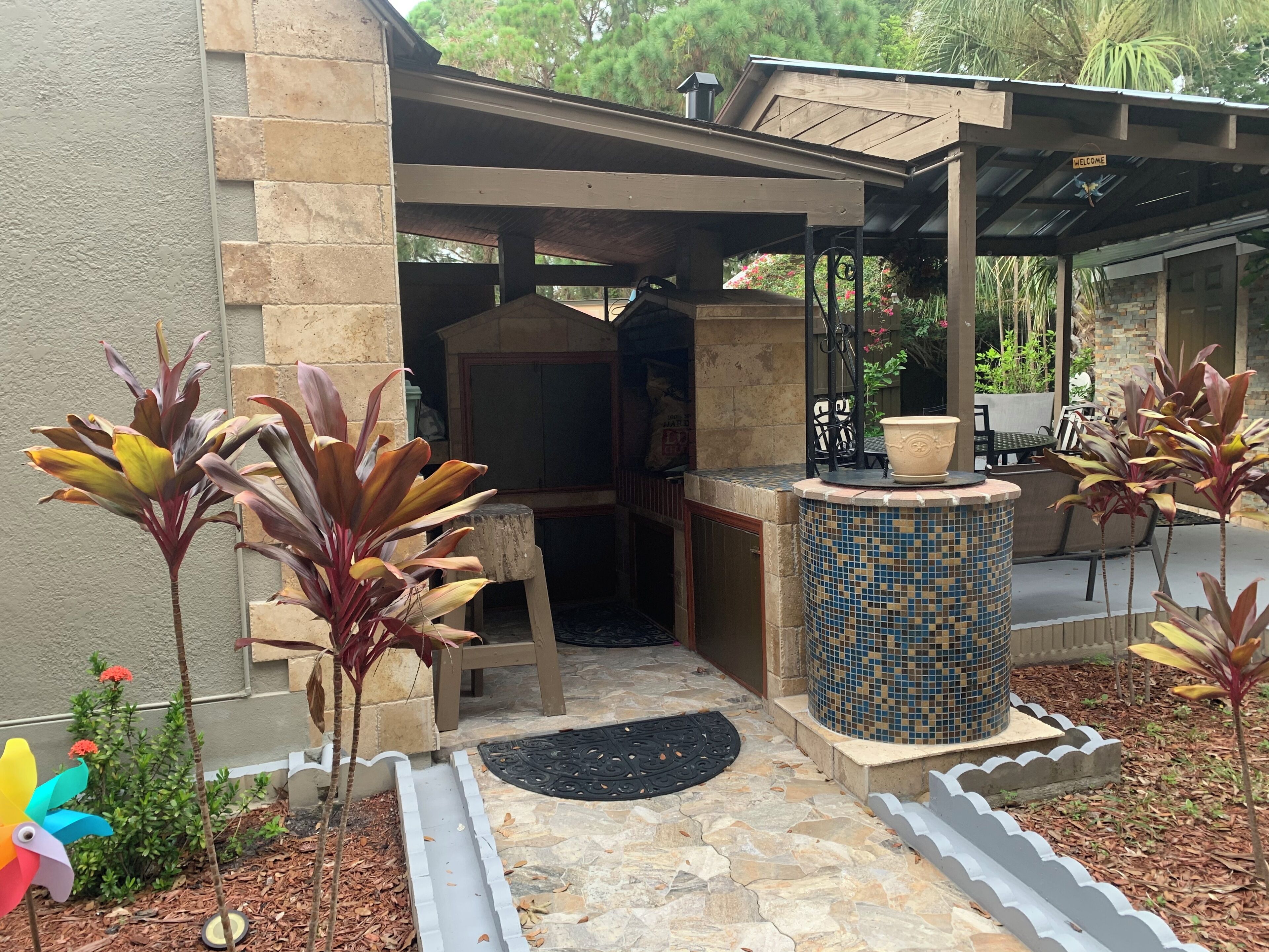 A covered outdoor area with a stone wall, a tiled column, and potted plants.. Eirini’s Home