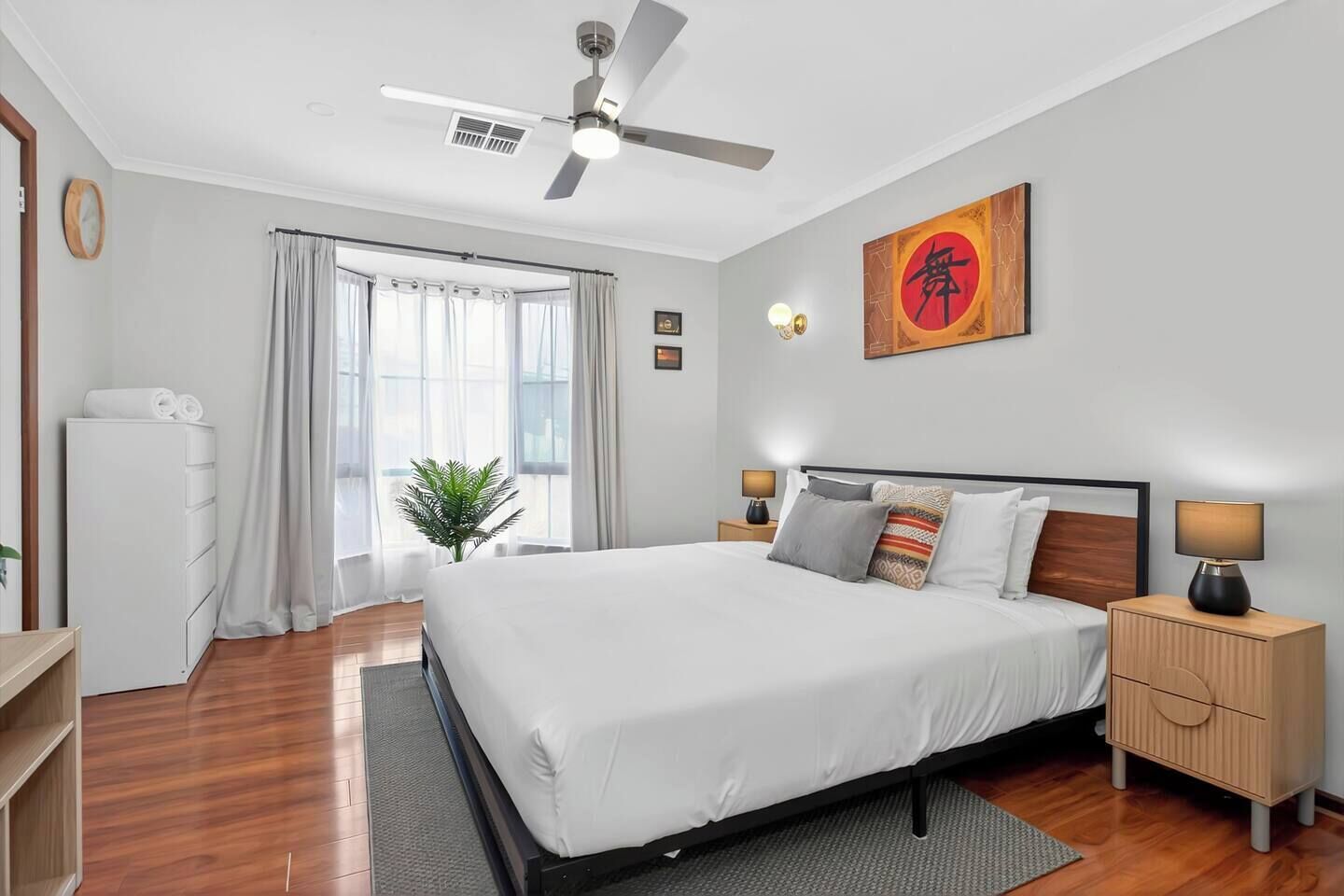 Une chambre moderne avec un lit, des tables de chevet, un ventilateur de plafond et une fenêtre avec des rideaux.