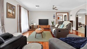 A modern living room with a flat-screen TV, two sofas, a coffee table, and a ceiling fan. - Hallett Horizon Explore Clifftops Coast and Trails (Hallett Cove)