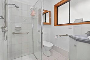 Et moderne badeværelse med brusekabine i glas, toilet, vask med underskab og et spejl over vasken.