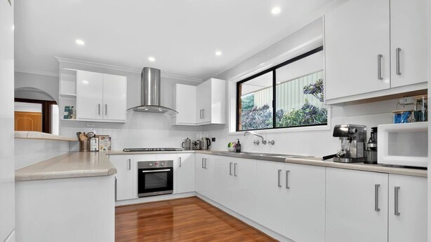 A modern kitchen with white cabinets, a stainless steel range hood, a built-in oven, a window with a view of greenery, and a countertop with a coffee machine. - Hallett Horizon Explore Clifftops Coast and Trails (Hallett Cove)