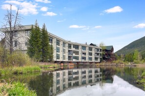 A multi-story building with a reflection in a calm body of water, surrounded by greenery and a mountain in the background. - Perfect Keystone Ski Home: 2 Min Walk to Gondola! (Keystone)