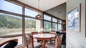 A dining area with a round table and chairs, large windows with a view of a forest, and a stone wall. - Beautiful Keystone Condo: Perfect Leaf Peeping! (Keystone)