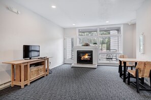 A modern living room with a fireplace, a television, a dining area, and a large window. - Beautiful Keystone Condo: Perfect Leaf Peeping! (Keystone)
