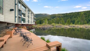 A wooden deck with outdoor seating, overlooking a calm lake and forested hills. - Beautiful Keystone Condo: Perfect Leaf Peeping! (Keystone)