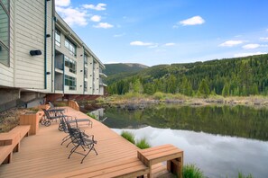 A wooden deck with outdoor seating, overlooking a calm lake and forested hills. - Beautiful Keystone Condo: Perfect Leaf Peeping! (Keystone)