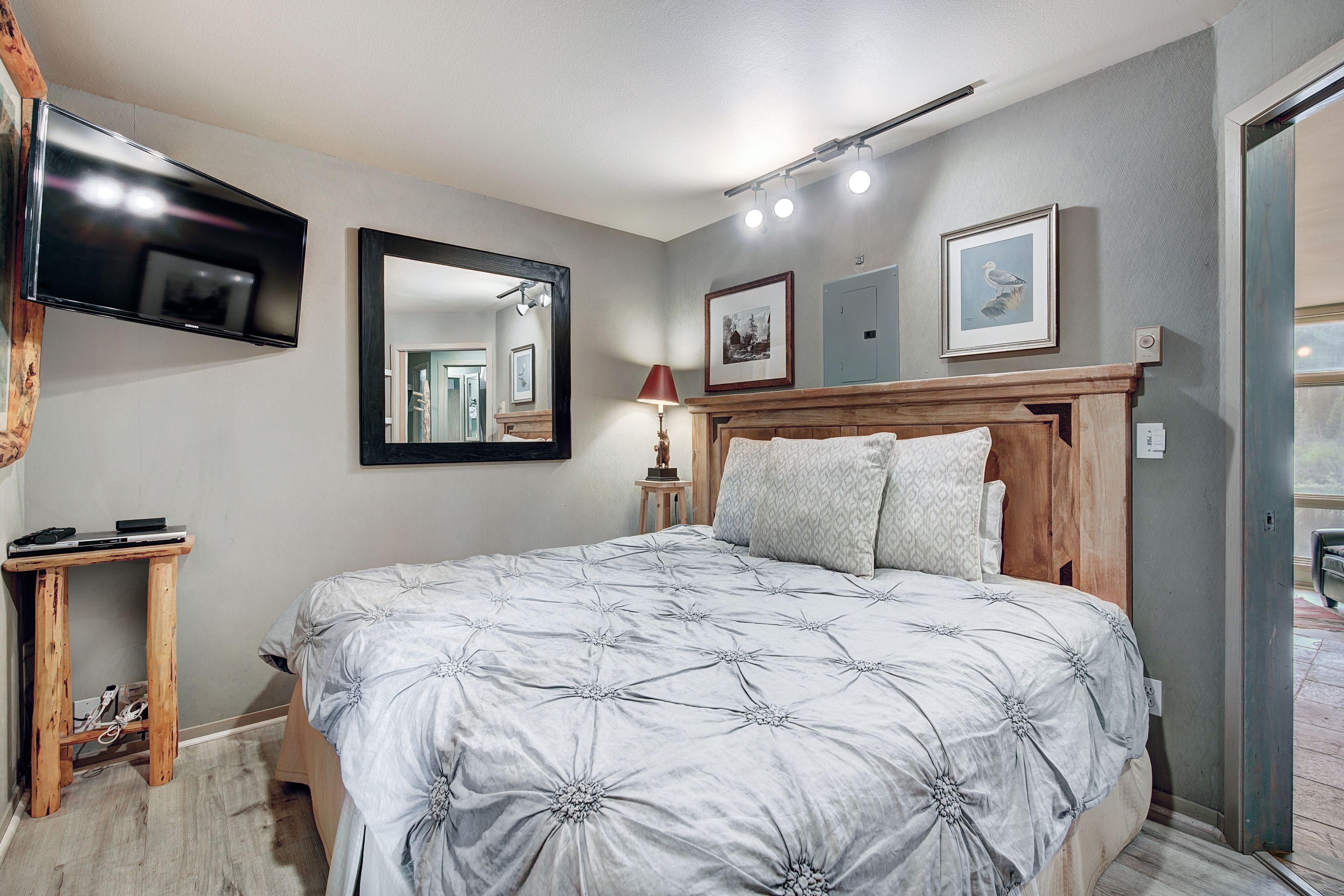 A bedroom with a bed, a TV mounted on the wall, a mirror, and framed pictures.