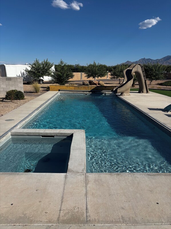 A swimming pool with a slide, a concrete deck, and a desert landscape in the background. - Fantastic 5-br, 3.5ba house with pool, hot tub AC located in Graham county, AZ. (Pima)