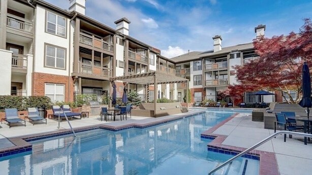 A swimming pool with lounge chairs and umbrellas, surrounded by multi-story buildings with balconies. - Cozy Perimeter Unit with resort-style pool (Dunwoody)