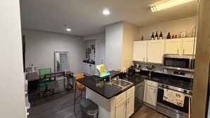 A modern kitchen with white cabinets, a black countertop, and stainless steel appliances. - Cozy Perimeter Unit with resort-style pool (Dunwoody)