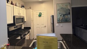 A kitchen with white cabinets, a microwave, a stove, a sink, and a countertop with a blue cutting board. - Cozy Perimeter Unit with resort-style pool (Dunwoody)