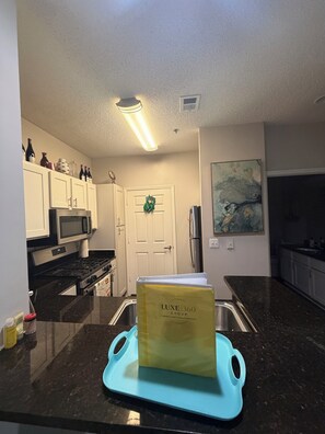 A kitchen with white cabinets, a microwave, a stove, a sink, and a countertop with a blue cutting board.