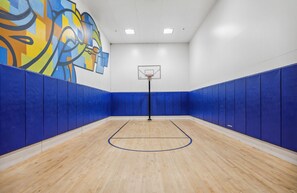 An indoor basketball court with blue padded walls, a wooden floor, and a basketball hoop.