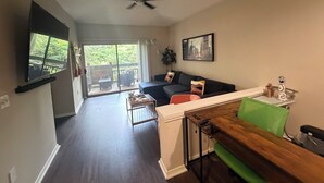 A living room with a sofa, a coffee table, a TV mounted on the wall, a ceiling fan, and a sliding glass door leading to an outdoor area. - Cozy Perimeter Unit with resort-style pool (Dunwoody)