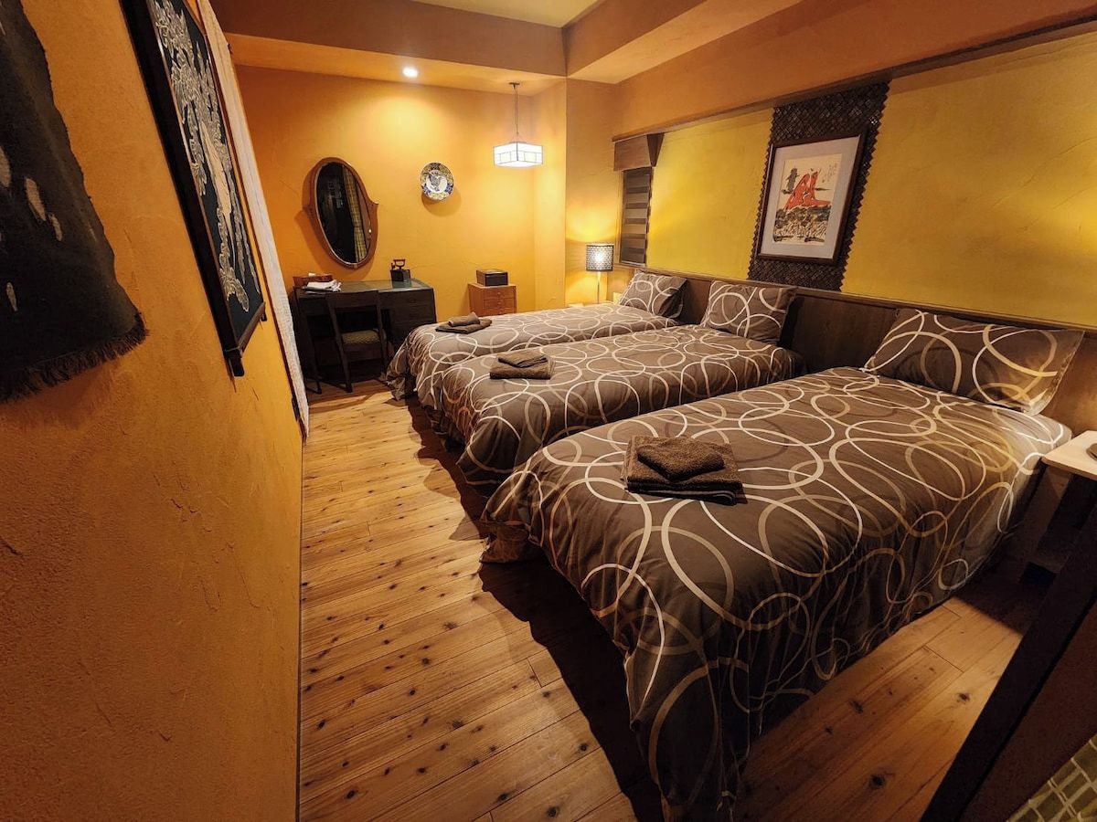 A hotel room with two beds, a desk, a chair, a lamp, and a framed picture on the wall.