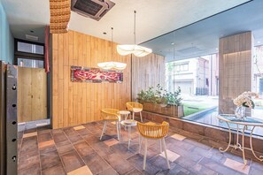 Ein modernes Interieur mit einer Holzwand, einem Essbereich mit Korbstühlen, einem Glastisch und einer Hängelampe.