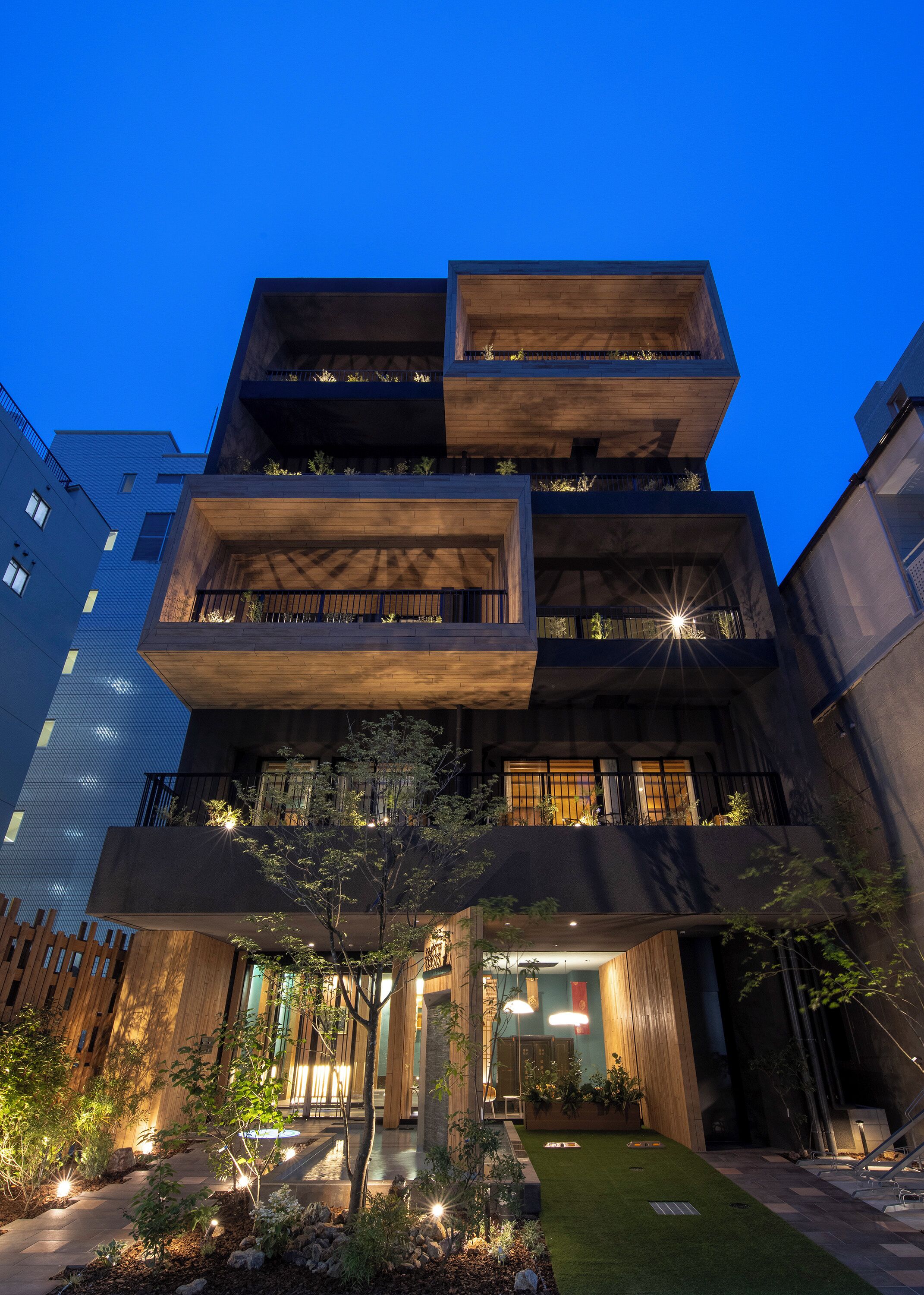 Un edificio a più piani con balconi, un'area giardino e un vialetto che conduce all'ingresso.
