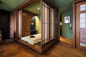 A traditional Japanese-style room with tatami flooring, a low platform bed, sliding doors, and a small shelf with a mirror and picture frame. - Spacious & Serene 84 ㎡ Retreat near Dotonbori, Kuromon Market & Shinsaibashi (大阪市)