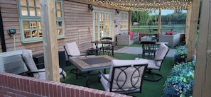 A covered patio with outdoor furniture, a table, and a view of a green field. - Marshland Alpacas Glamping Lodge (Barrow-upon-Humber)