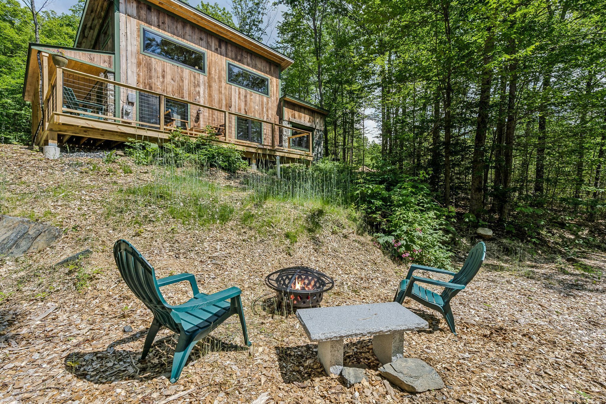 Une cabane en bois avec une terrasse, deux chaises, une table et un foyer.