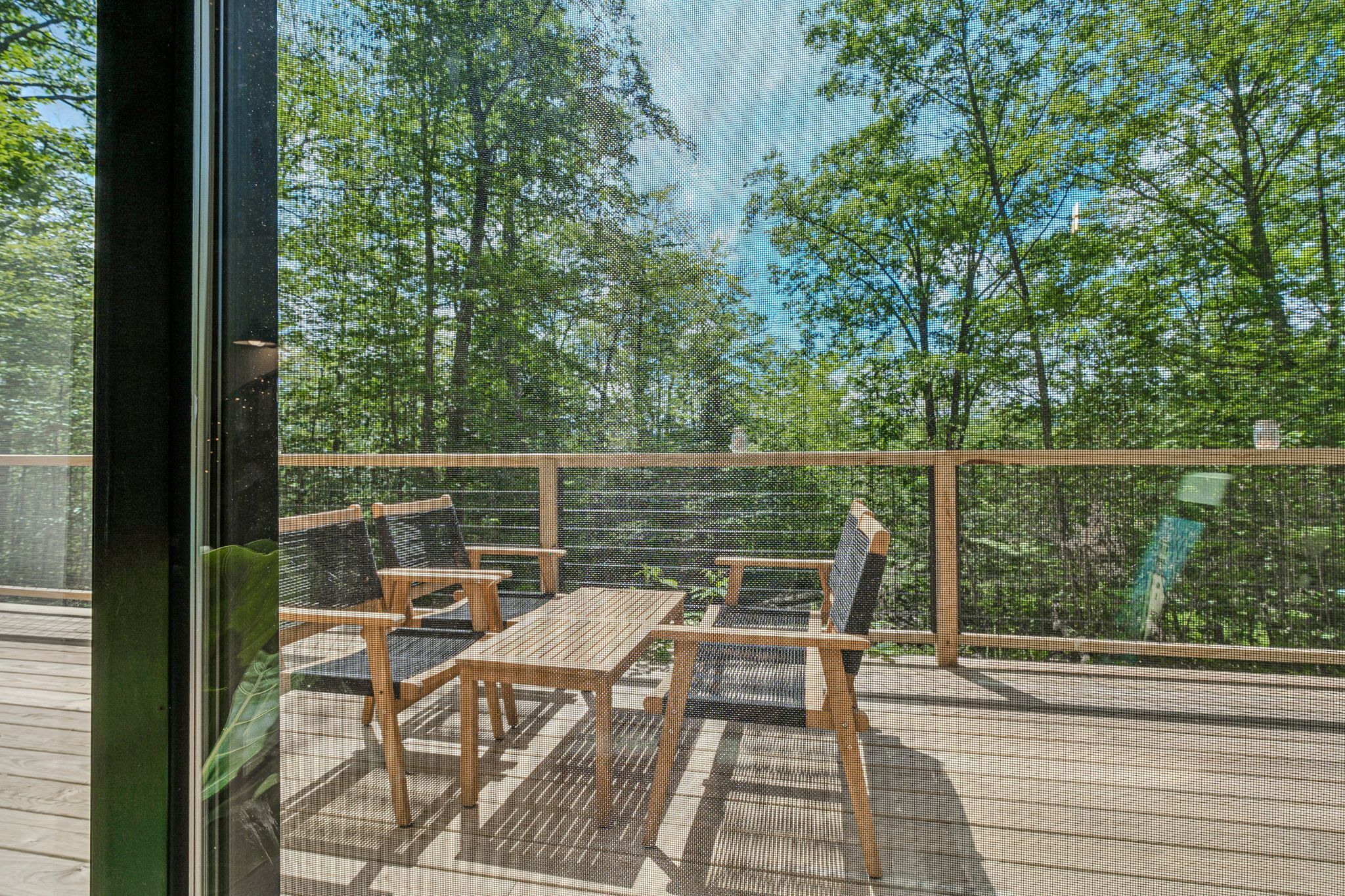 A deck with wooden furniture and a view of trees.