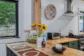 A kitchen with a window view, a toaster, a kettle, and a bowl of pinecones. - Gratitude Cottage, Quiet Nature Escape (Strafford)