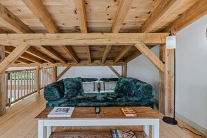 A wooden ceiling structure, a green velvet sofa with cushions, a white table with a book and a glass, and a floor lamp. - Gratitude Cottage, Quiet Nature Escape (Strafford)