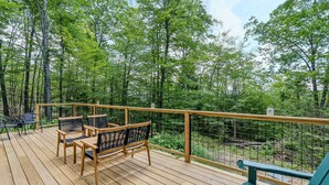 Um deck de madeira com móveis de exterior, guarda-corpo e vista para uma floresta.