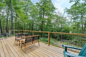 Eine Holzterrasse mit Gartenmöbeln, einem Geländer und Blick auf einen Wald.