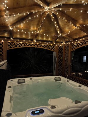 Ett bubbelbad under en pergola av trä, dekorerat med ljusslingor.