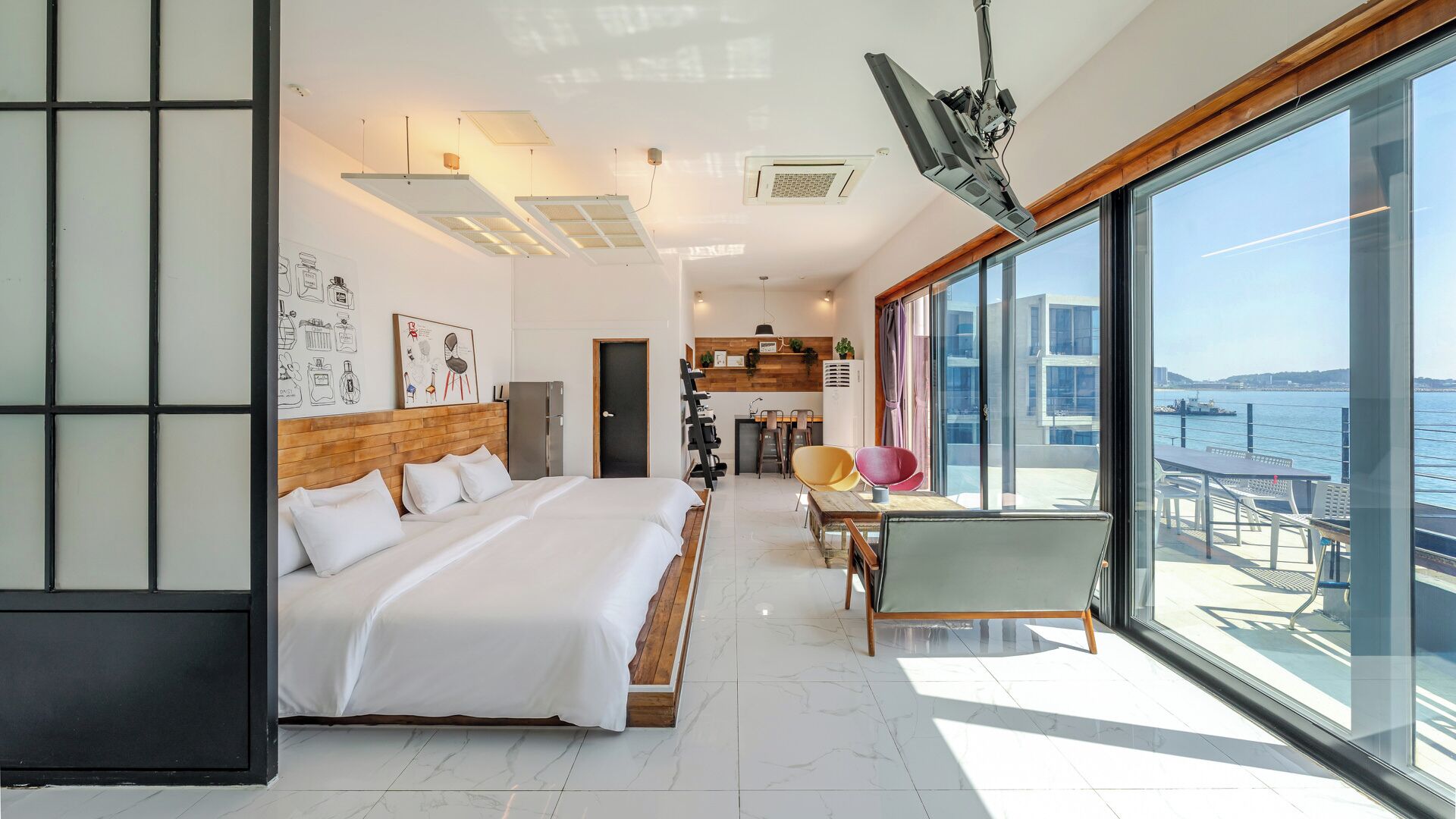Habitació d'hotel moderna amb un llit gran, zona de menjador i balcó amb vista al mar.
