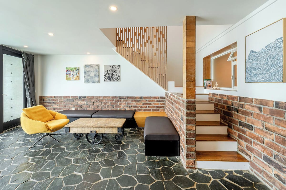 Un interior moderno con suelo de piedra, una escalera de madera, un banco y una silla amarilla.