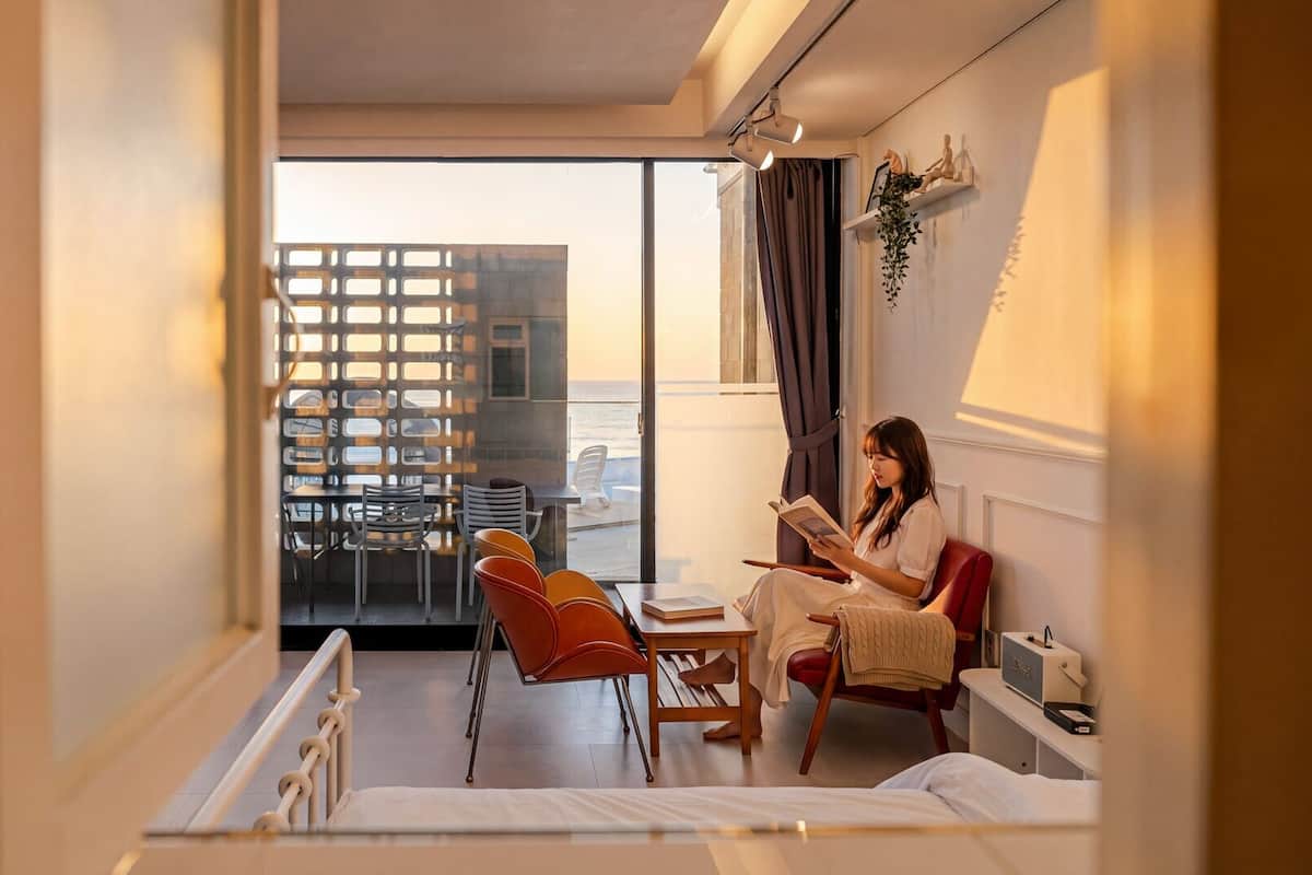 Una habitación de hotel con un ventanal grande, una cama, un sillón de lectura y una mesita.