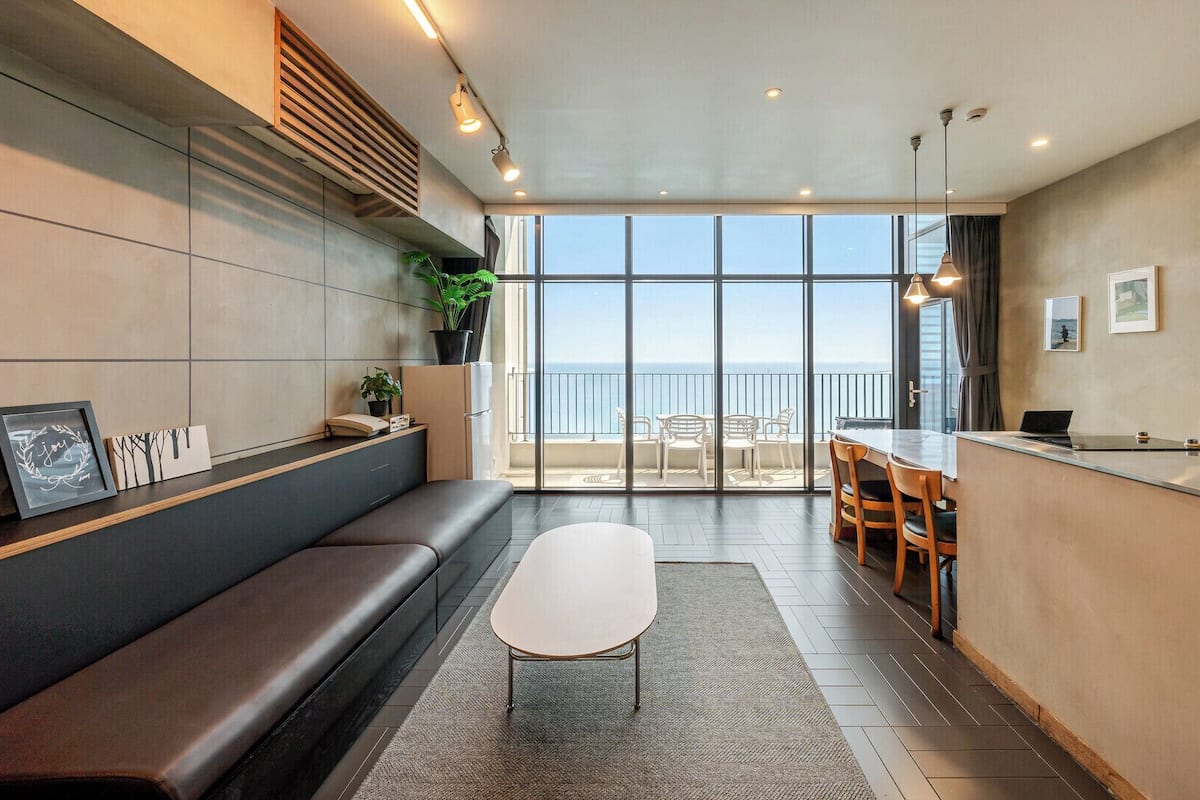 Un interior moderno con un banco, una mesita y vista al mar.