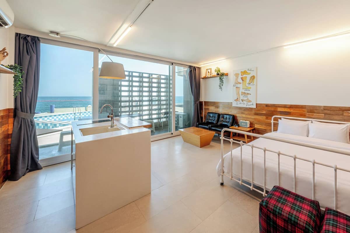 Habitación de hotel con cama, escritorio, silla, una mesita y vista al océano.