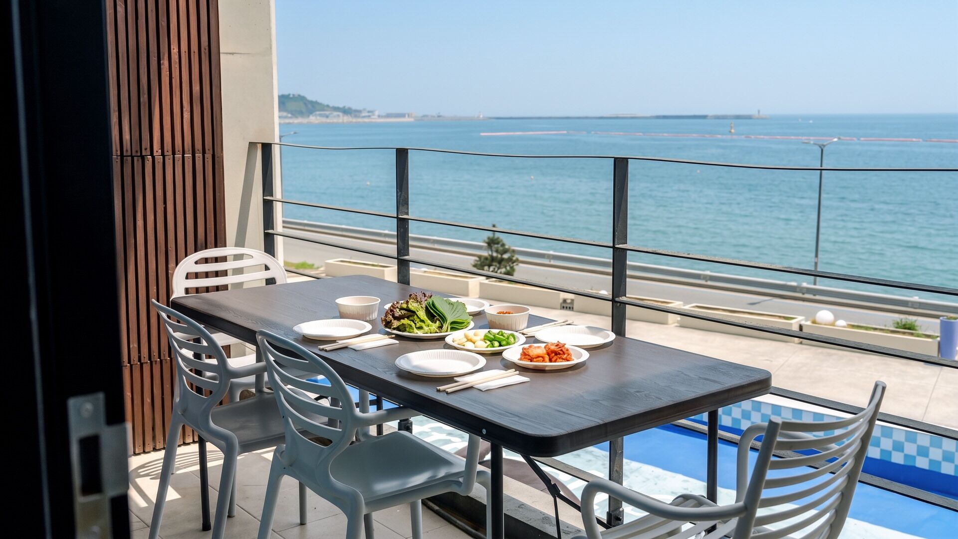 A balcony with a table set for dining, overlooking a body of water.