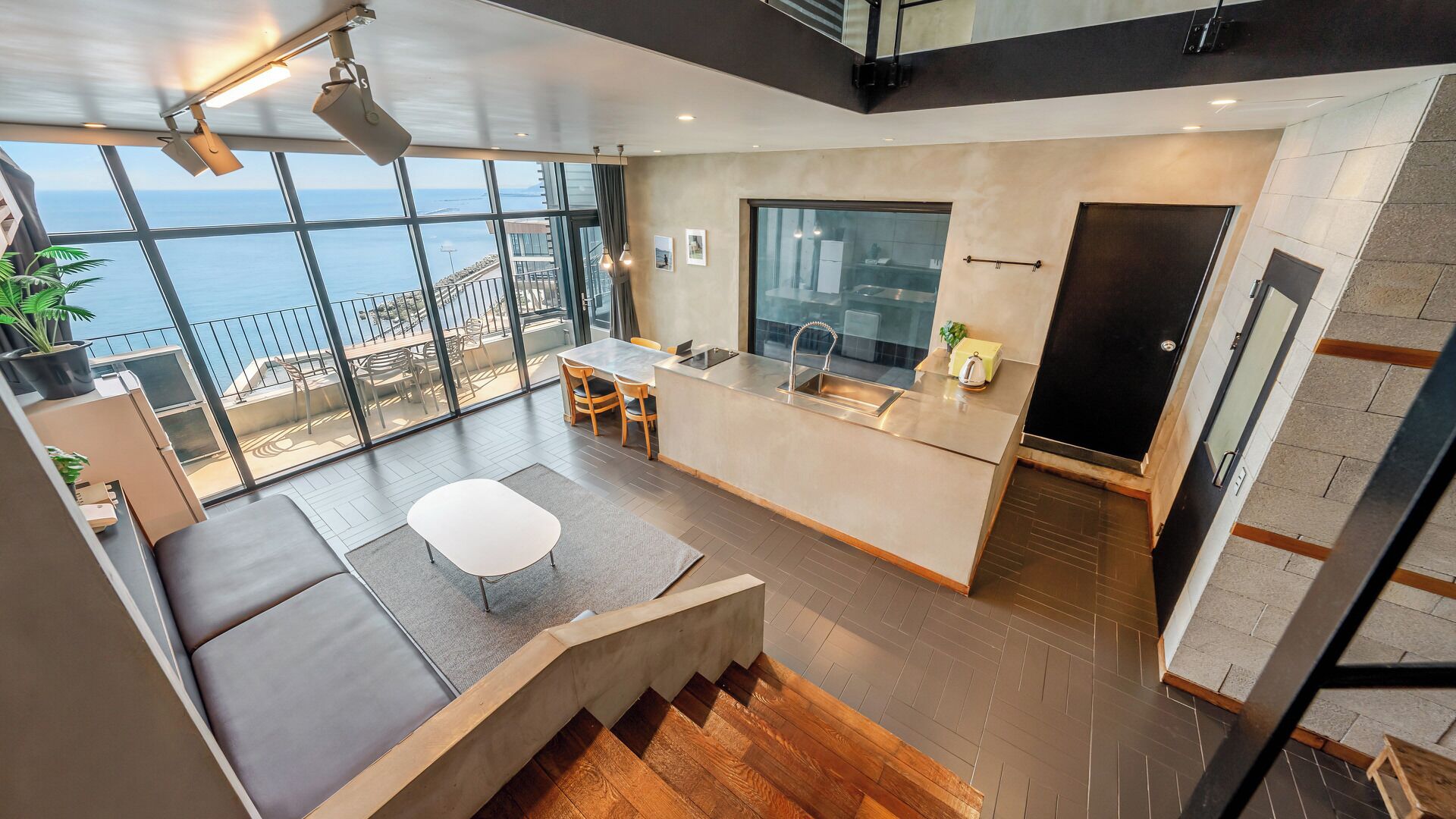 A modern kitchen with a large window, a dining area with a white table and chairs, and a view of the sea.