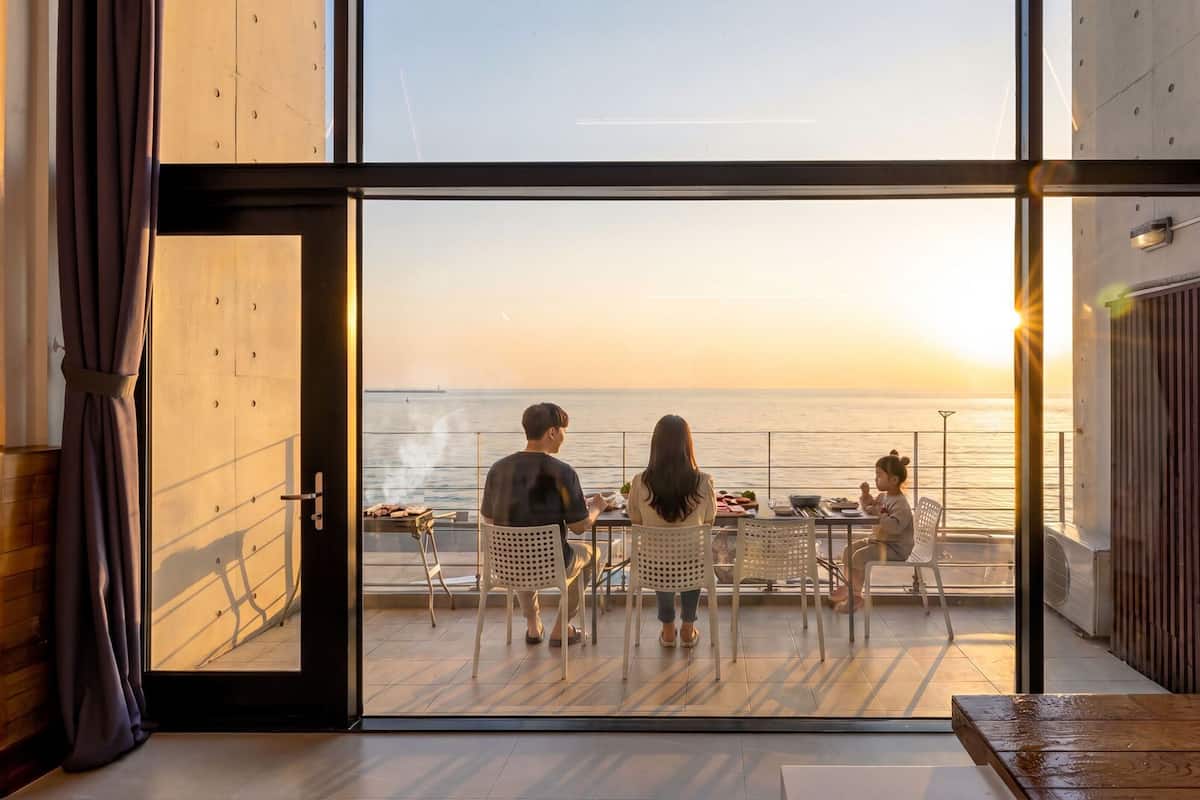 Un balcón abierto con vistas al mar, una mesa con sillas y una parrilla.