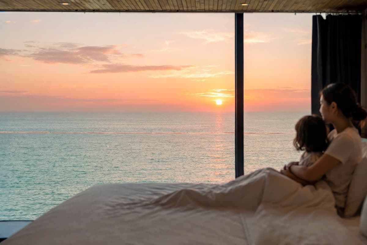 Un dormitorio con un ventanal grande que da al mar al atardecer.