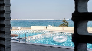 Una piscina con diseño a cuadros, vista al mar y un árbol.