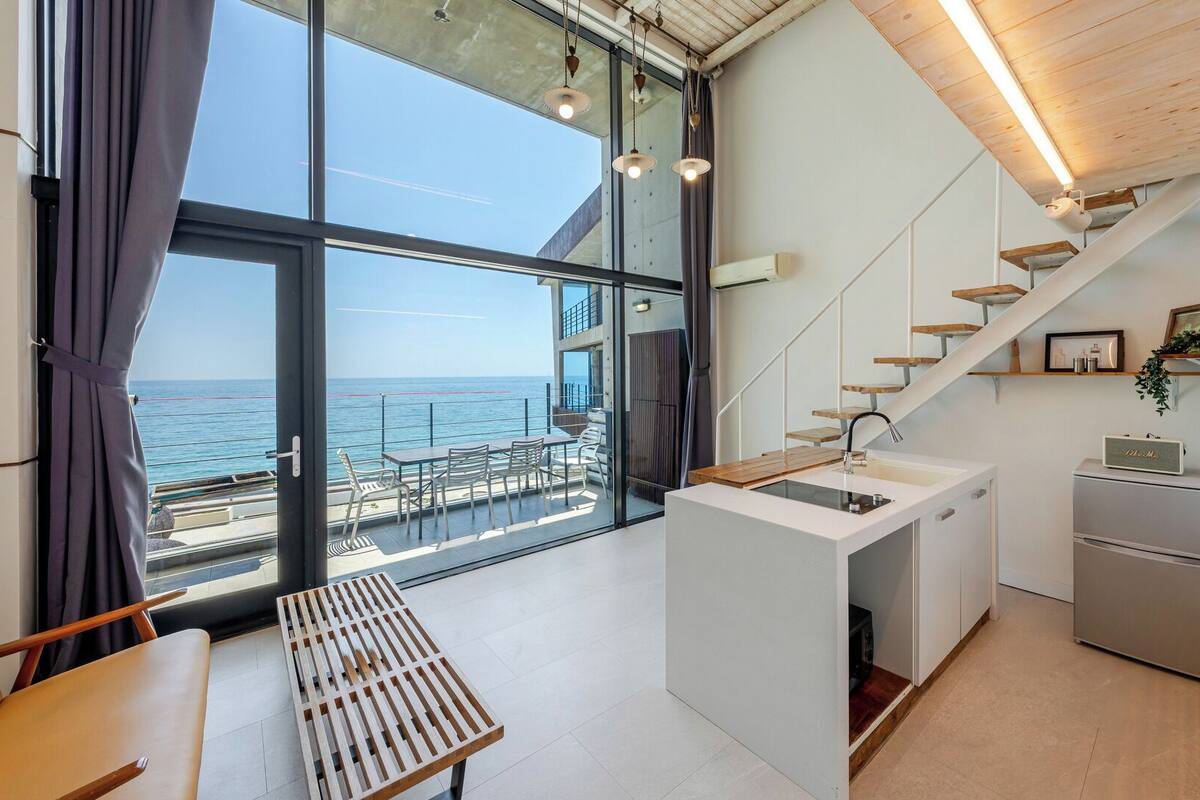 Una cocina moderna con vista al mar, un comedor con banco y una escalera de madera.