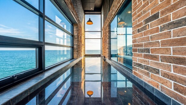 A corridor with large windows, a reflective floor, and a brick wall. - Uljin French Paper Pension (Uljin)